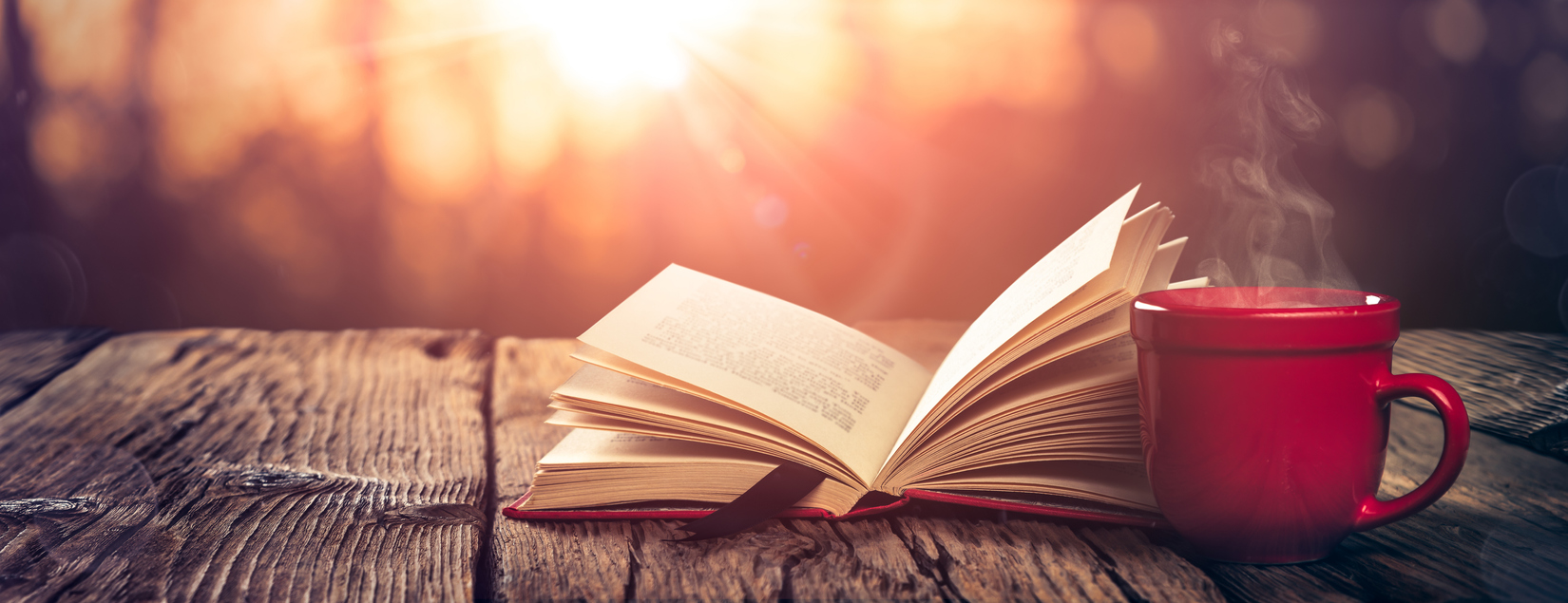 Open Book And Steaming Cup Of Coffee On Wooden Table