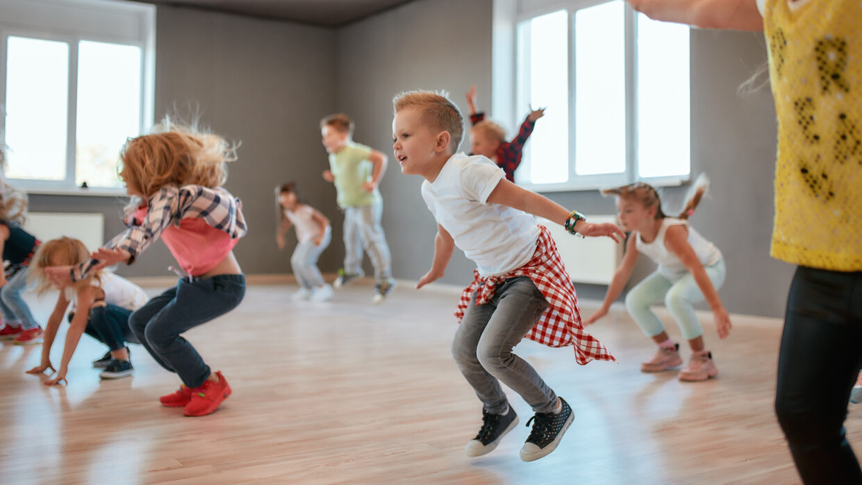Group Of Cute Little Boys And Girls Studying Modern Dance In Studio. Children Jumping While Having A Choreography Class